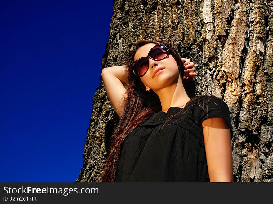 Close up of girl in glasses next to a tree.