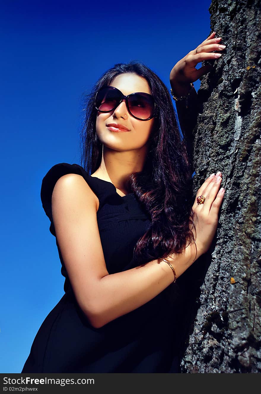 Glamoure lady in black dress next to a tree.