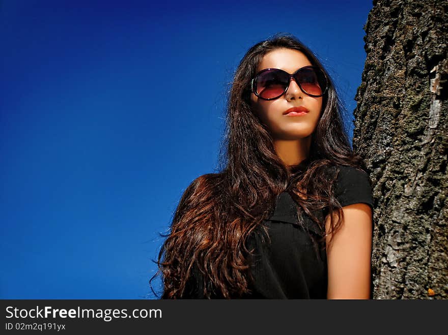 Glamoure lady in black next to a tree.