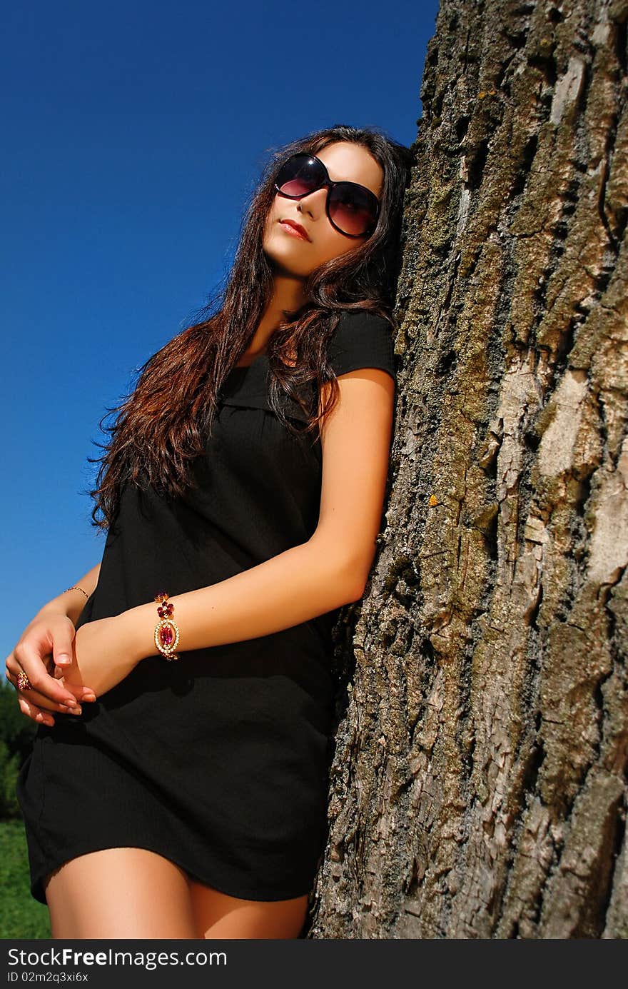 Glamoure lady in black dress next to a tree.