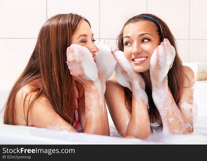 Two tricksy beautiful women in jacuzzi with foam on hands