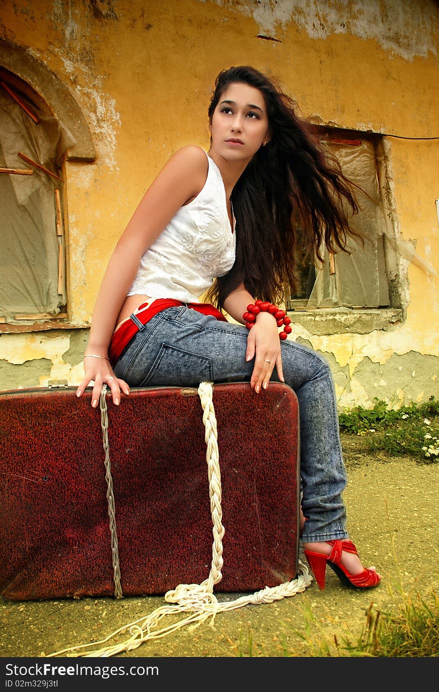 Beautiful model sitting on red suitcase.