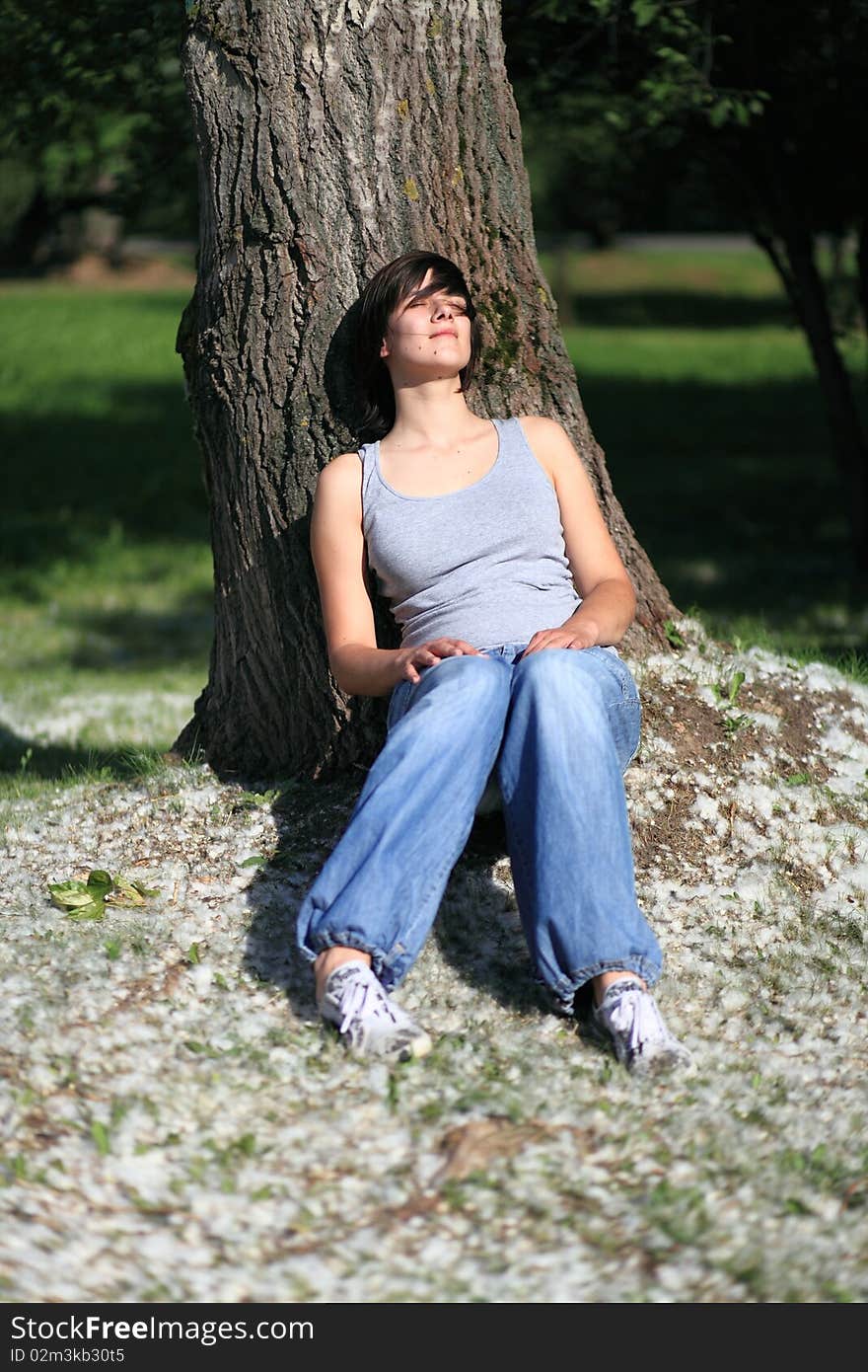 Close-up portrait of young woman taking sun and relaxing sitting under poplar tree. Close-up portrait of young woman taking sun and relaxing sitting under poplar tree