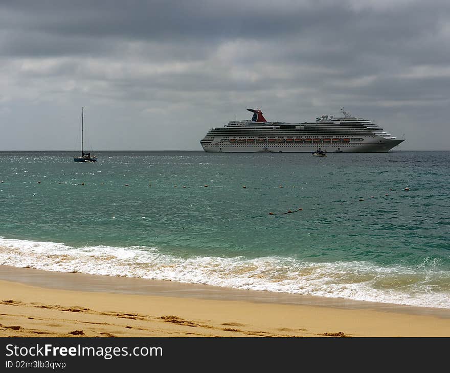 Huge cruise ship anchoring outside the harbor in front of the beach. Sky is cloudy with small patches of sun giving the ocean a beautiful green color. Huge cruise ship anchoring outside the harbor in front of the beach. Sky is cloudy with small patches of sun giving the ocean a beautiful green color