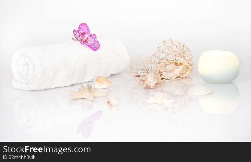 White towel with Orchid, Seashells and a lit candle on white with beautiful reflection. White towel with Orchid, Seashells and a lit candle on white with beautiful reflection.