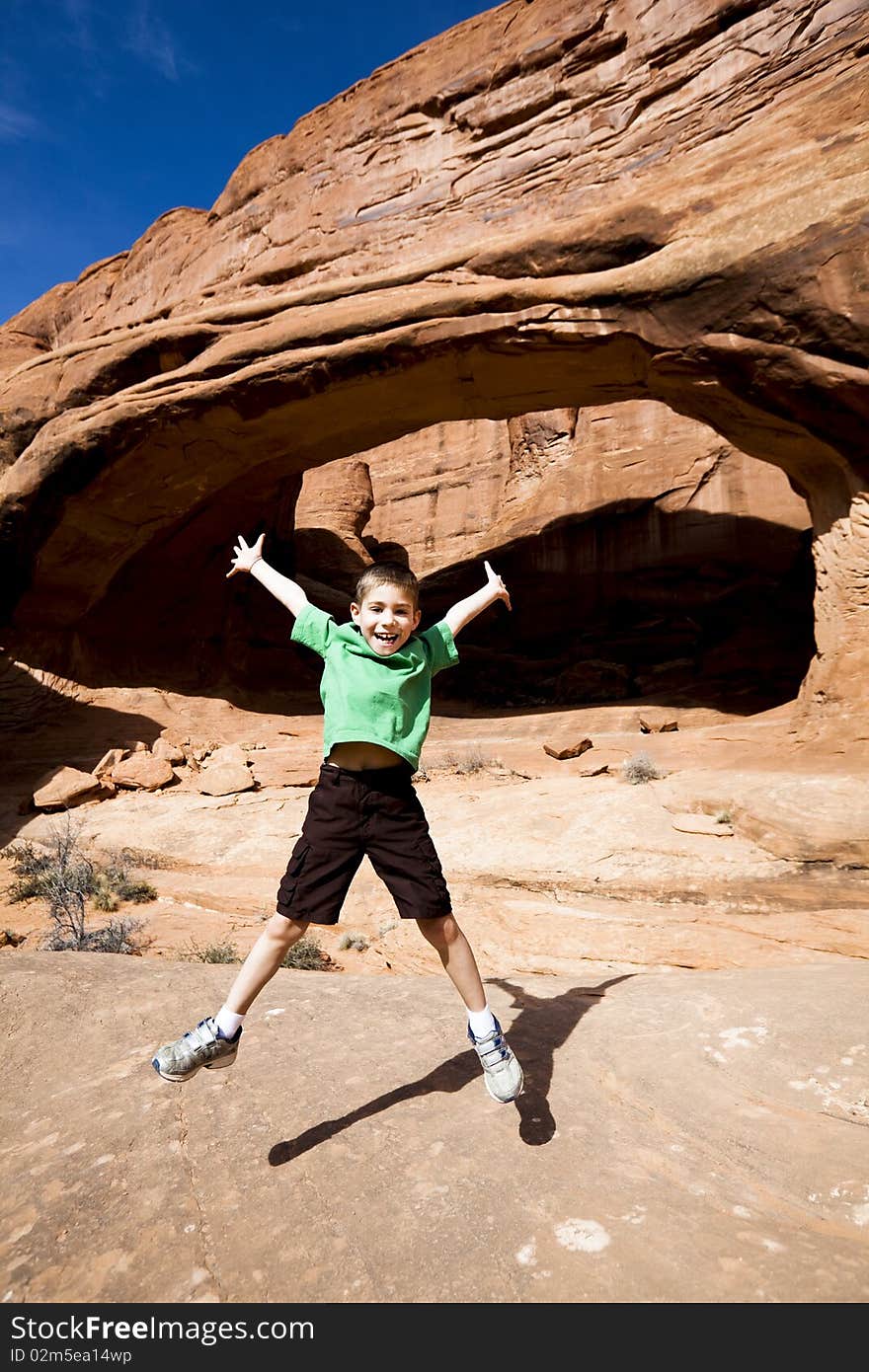 Young boy jumping with outstretched arms and legs while hiking in Arches National Park near Moab UT. Young boy jumping with outstretched arms and legs while hiking in Arches National Park near Moab UT