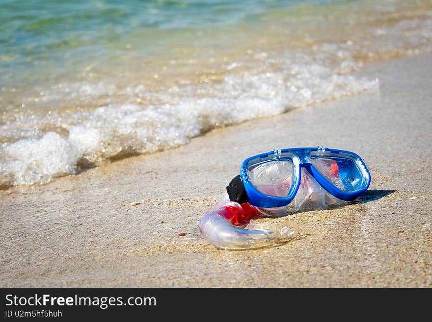 Mask and snorkel lying on sand of beach and washing by surf