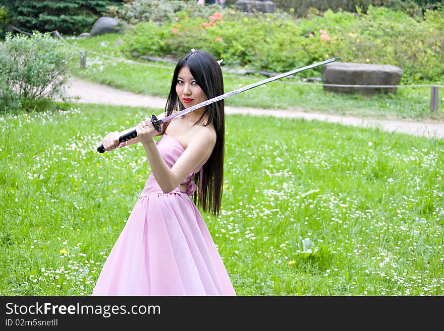 Beutiful japanese woman in pink dress wields a sword