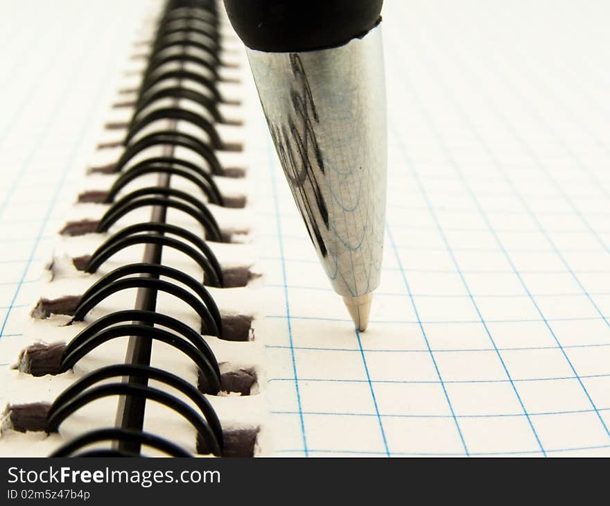 Darkenning ball-point pen on notebook in check which threaded spiraldarkenning ball-point pen on notebook in check which threaded spiral