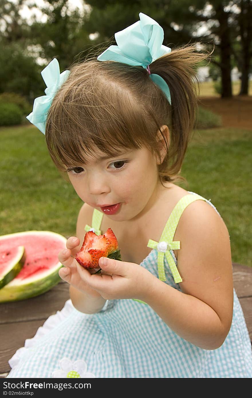 Little girl enjoying eating a huge red strawberry outdoors. Little girl enjoying eating a huge red strawberry outdoors.