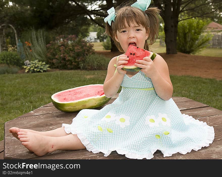 Small girl sitting on picnic table enjoying a large slice of watermelon. Small girl sitting on picnic table enjoying a large slice of watermelon.