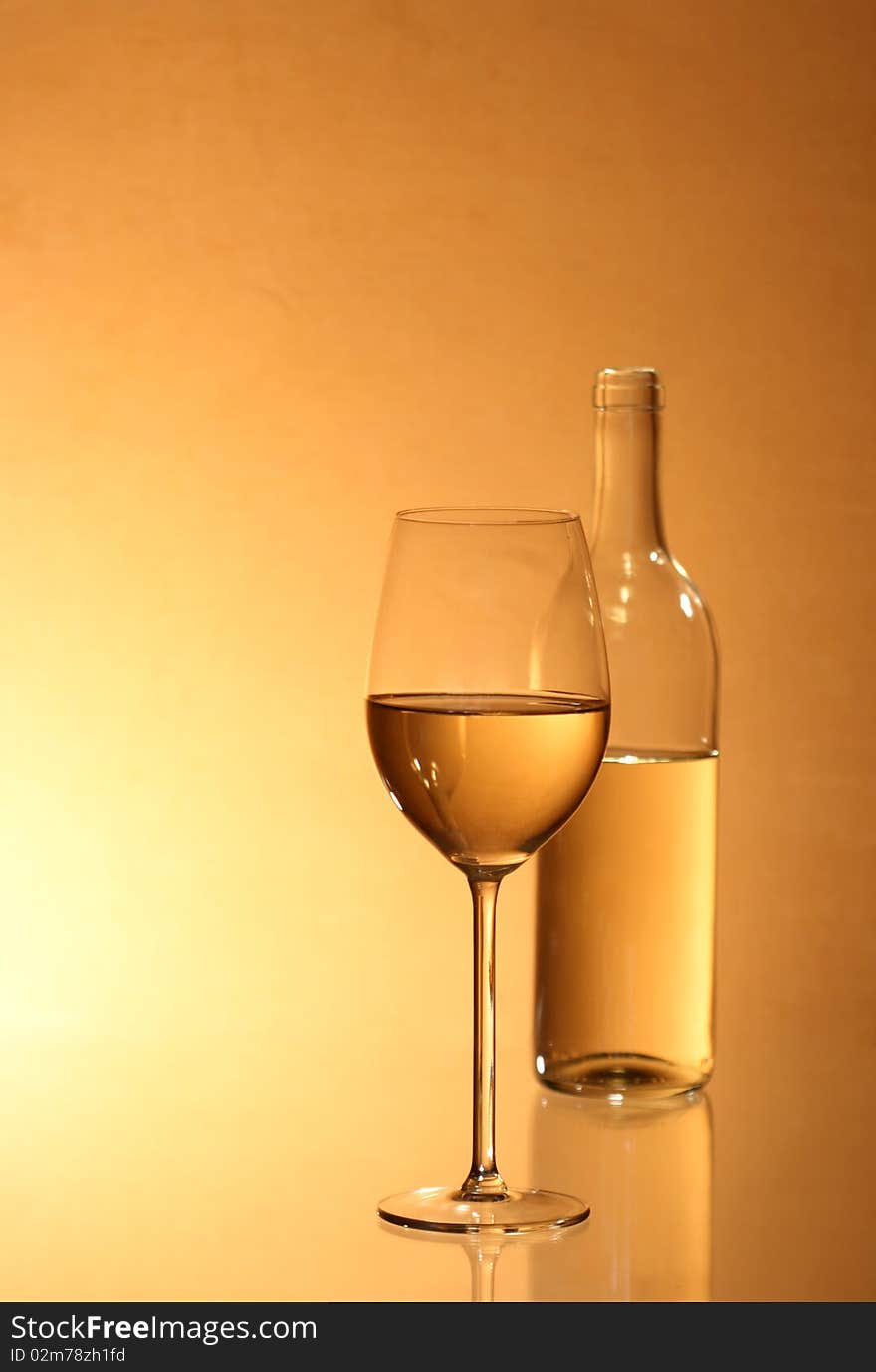 Wineglass near bottle of white wine with reverberation on red-yellow background