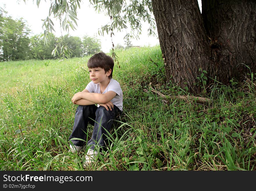 Child sitting under a tree on a green meadow. Child sitting under a tree on a green meadow