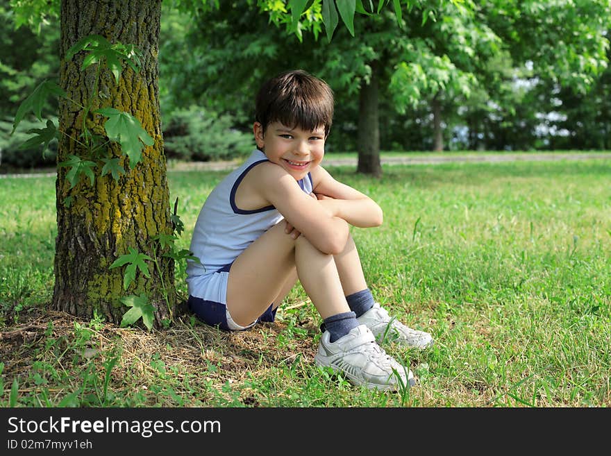 Smiling child sitting under a tree on a green meadow. Smiling child sitting under a tree on a green meadow