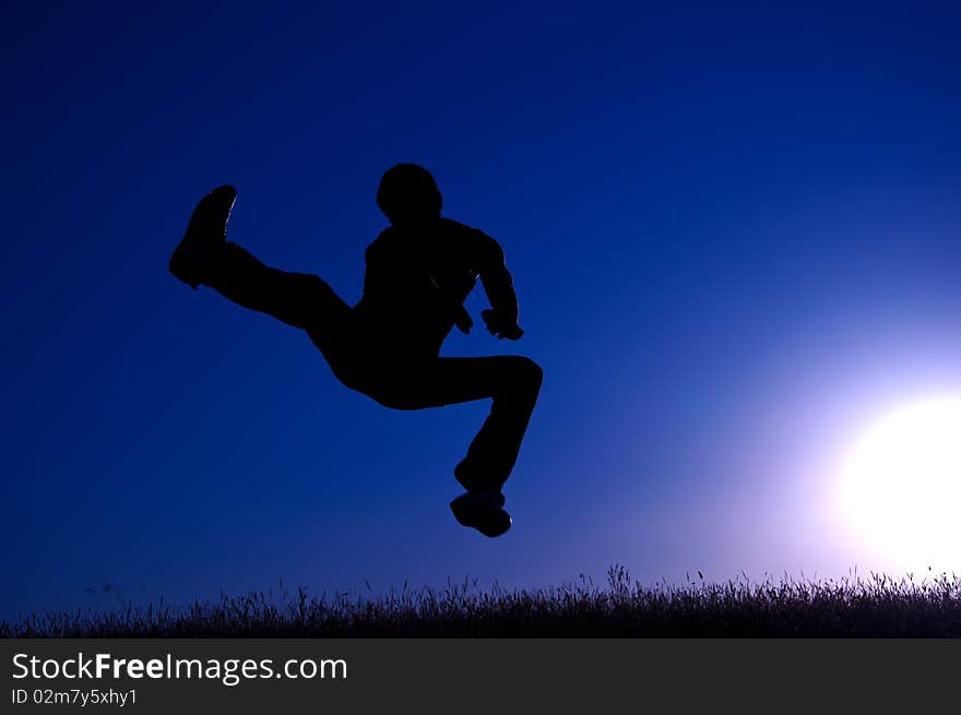 Black silhouette of a jumping young man on a blue sky and sun background. Black silhouette of a jumping young man on a blue sky and sun background