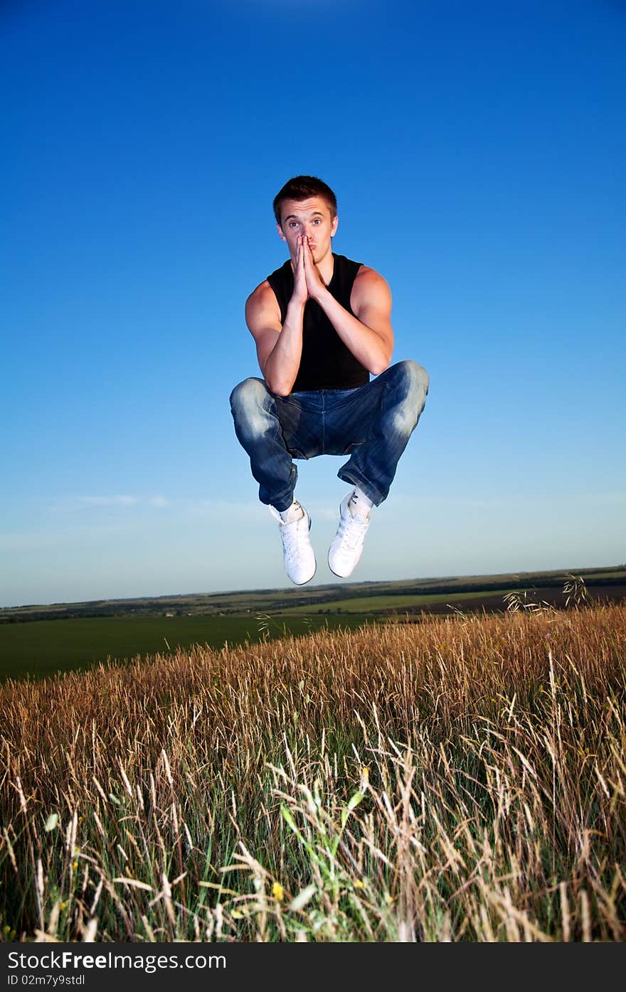 A young man hanging in the air above the meadow against the blue sky. A young man hanging in the air above the meadow against the blue sky