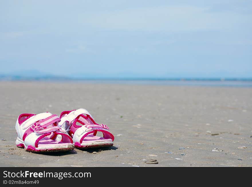 A young girl's sandals on the beach in the sand.