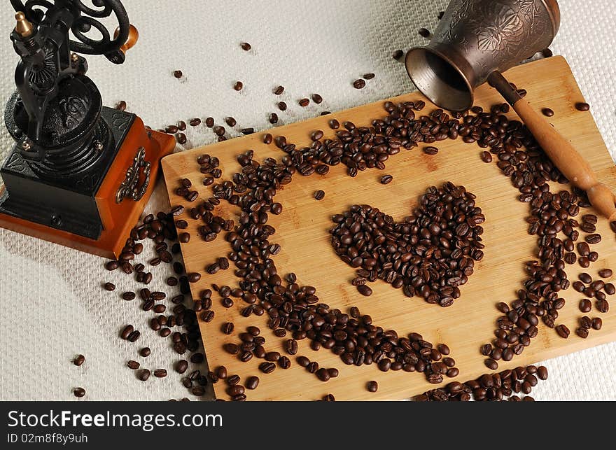 Coffee beans in a heart's shape on the breadboard with coffee mill and coffee pot