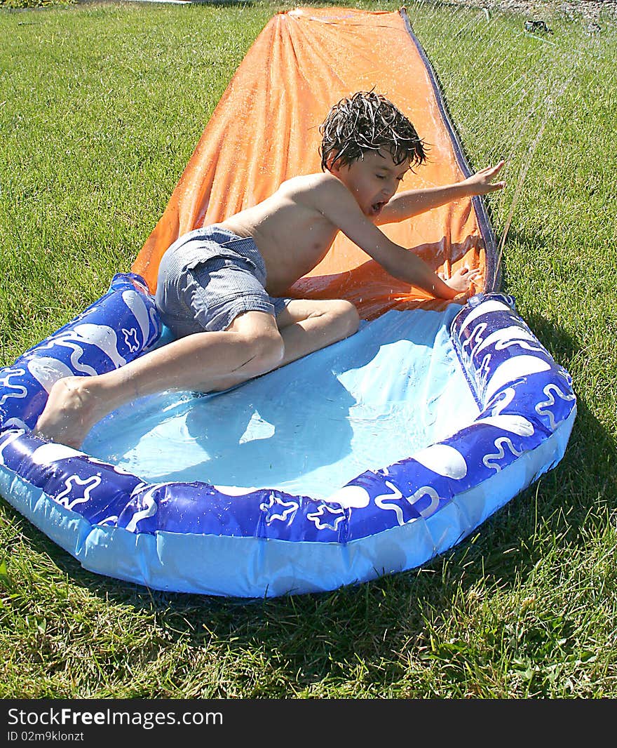 Boy riding down the water slide at home backyard. Boy riding down the water slide at home backyard.