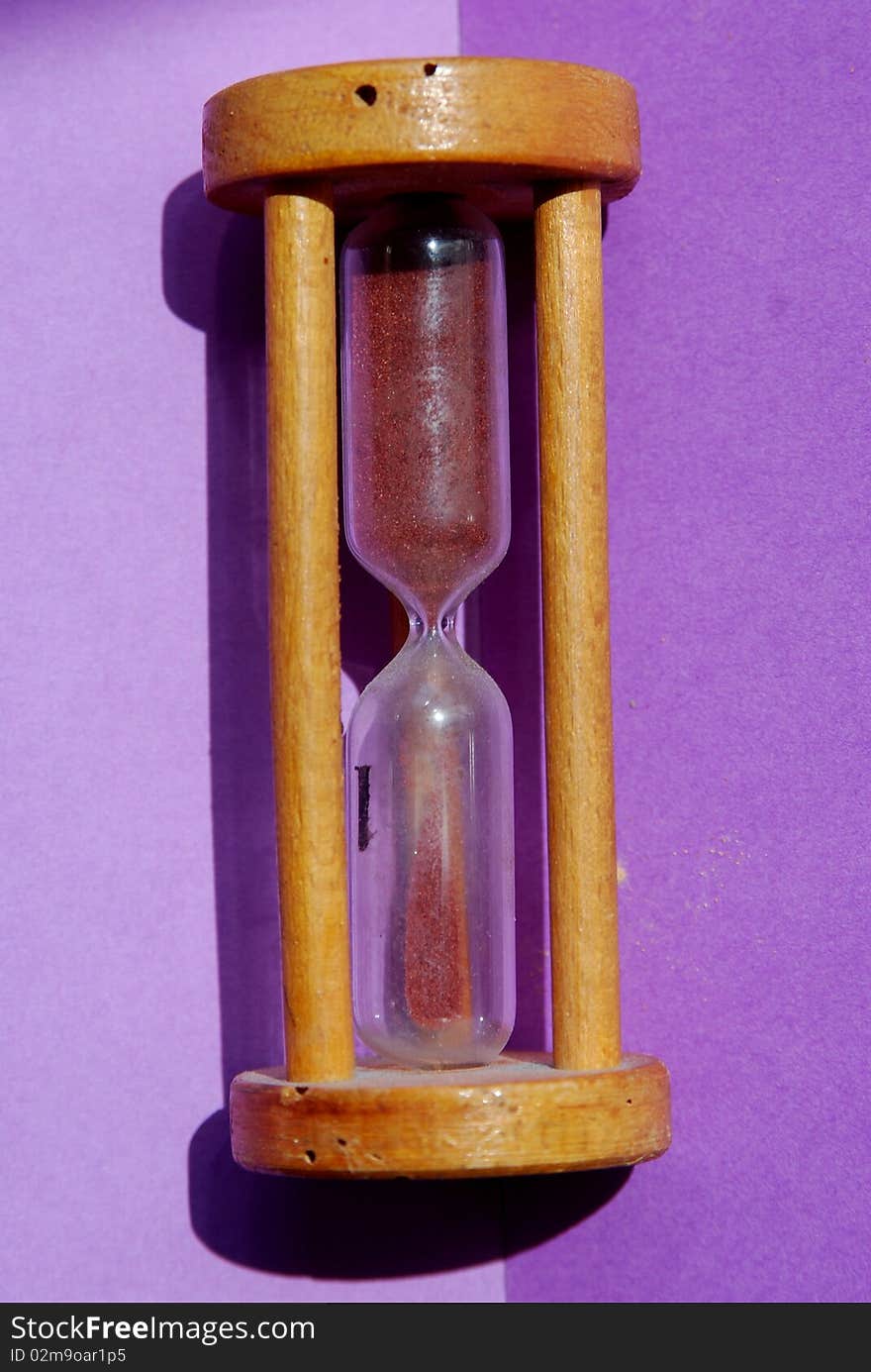 An old style wooden hourglass on a purple background