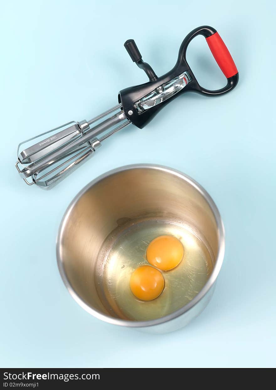 An egg beater eggs and a mixing bowl on a kitchen bench