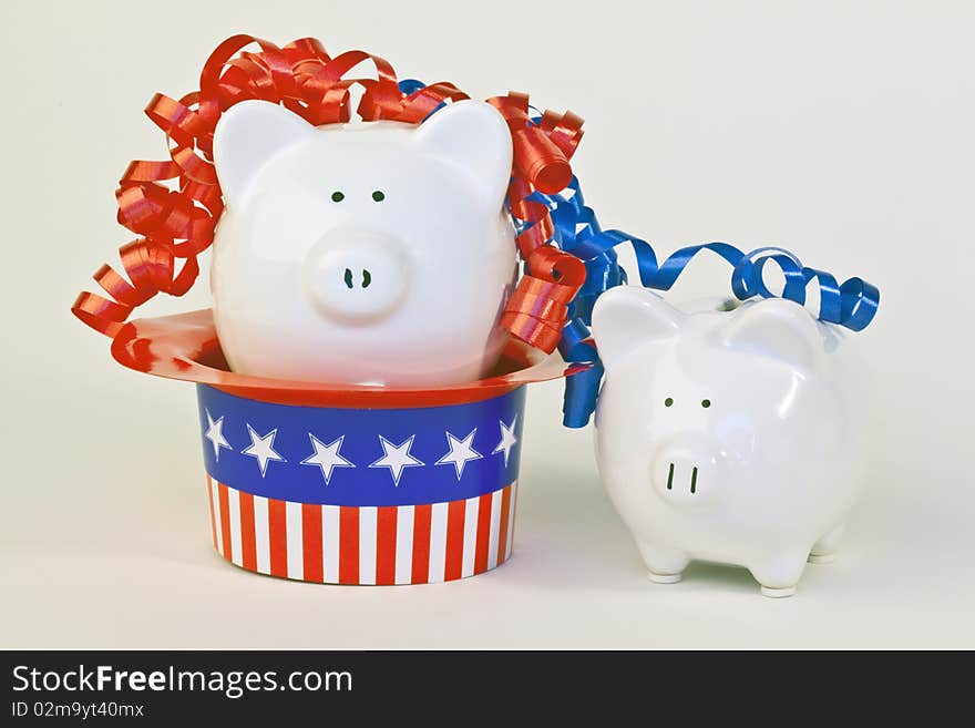 Two patriotic piggy banks, one sitting in a stars and stripes hat, with red and blue ribbon curls on a white background.