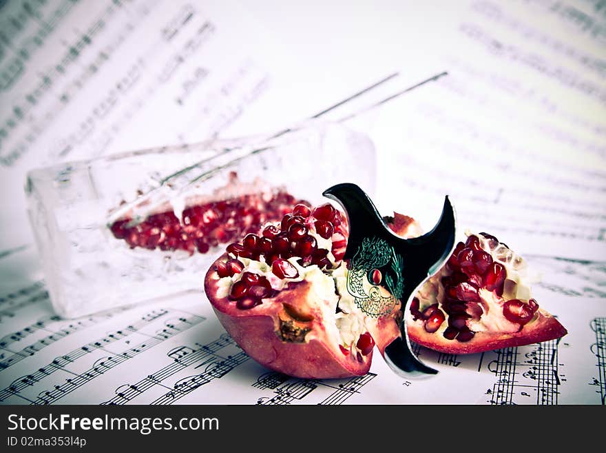 Red pomegranate pierced by shuriken on the music partiture sheets with the metal chopsticks and pomegranate grains in the ice vase. Red pomegranate pierced by shuriken on the music partiture sheets with the metal chopsticks and pomegranate grains in the ice vase