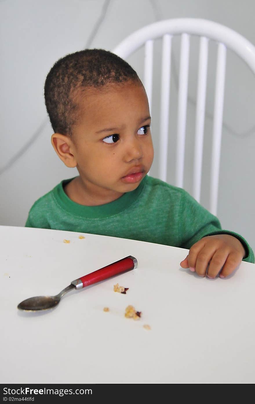 Child looking for more food while sitting at dinner table with spoon ready. Child looking for more food while sitting at dinner table with spoon ready