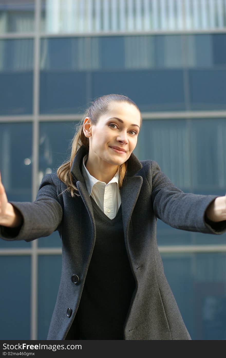 A young and attractive business woman in formal clothes is trying to embrace the camera man. The image is taken on a modern outdoor background. A young and attractive business woman in formal clothes is trying to embrace the camera man. The image is taken on a modern outdoor background.