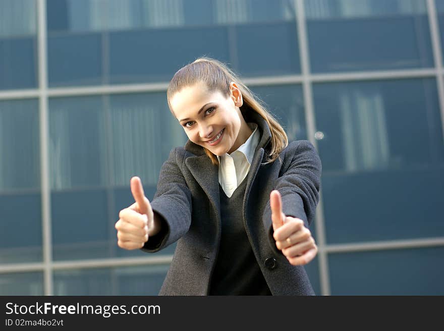 A young and attractive business woman in formal clothes is holding her thumbs up as a sign of success. The image is taken on a modern background. A young and attractive business woman in formal clothes is holding her thumbs up as a sign of success. The image is taken on a modern background.