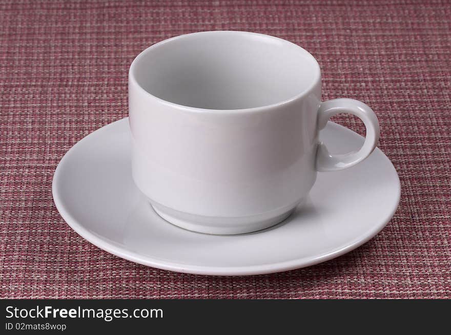 Little white coffee cup on a white saucer over checked table-cloth background