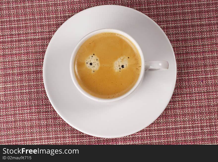 Little white espresso coffee cup on a white saucer over checked table-cloth background (upprer view)