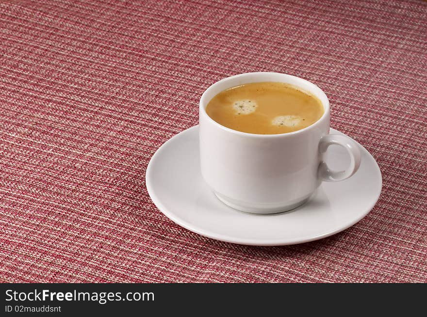 Little white espresso coffee cup on a white saucer over checked table-cloth background