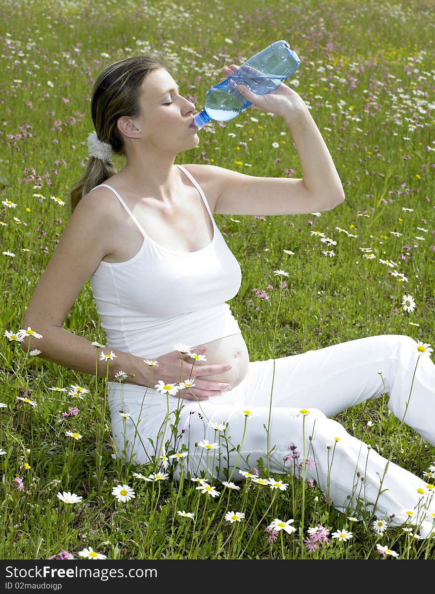 Pregnant woman on meadow with bottle of water