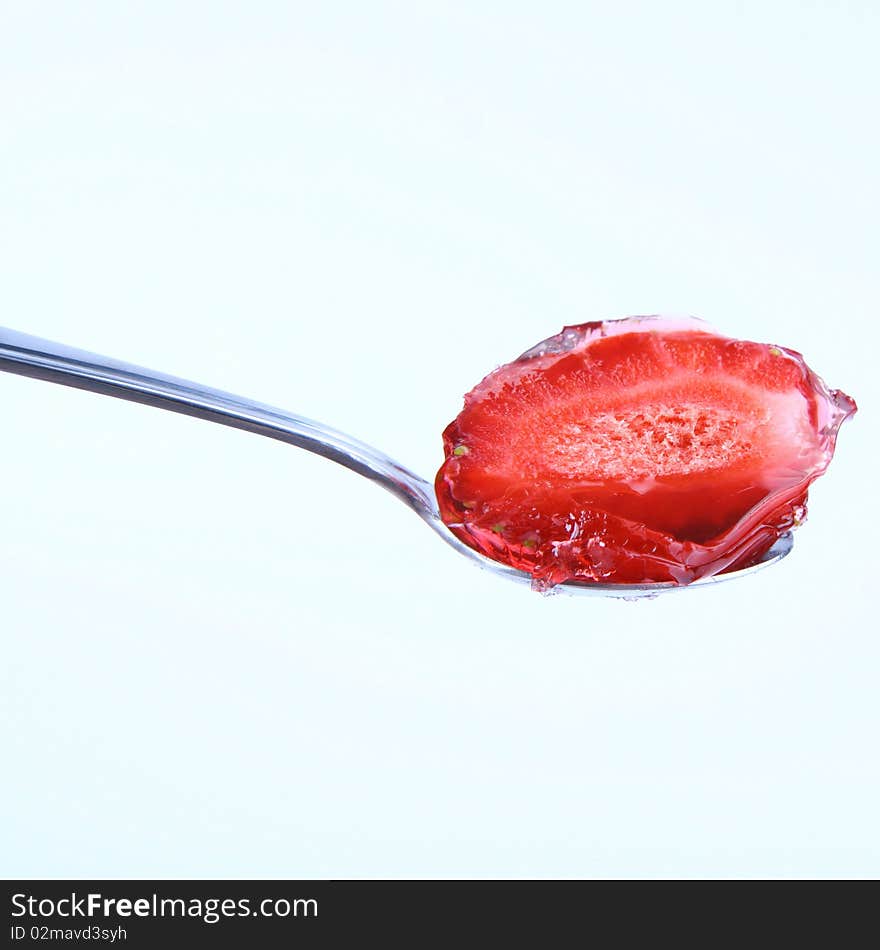 Piece of a strawberriey covered with jelly on a spoon