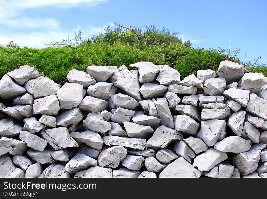 Traditional mediterranean stone wall with thick green bush. Traditional mediterranean stone wall with thick green bush