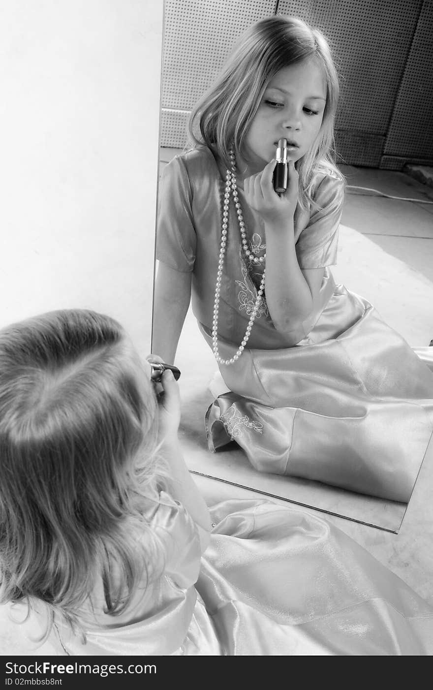 Little girl rouge lips and looking at mirror, studio photo, black and white portrait