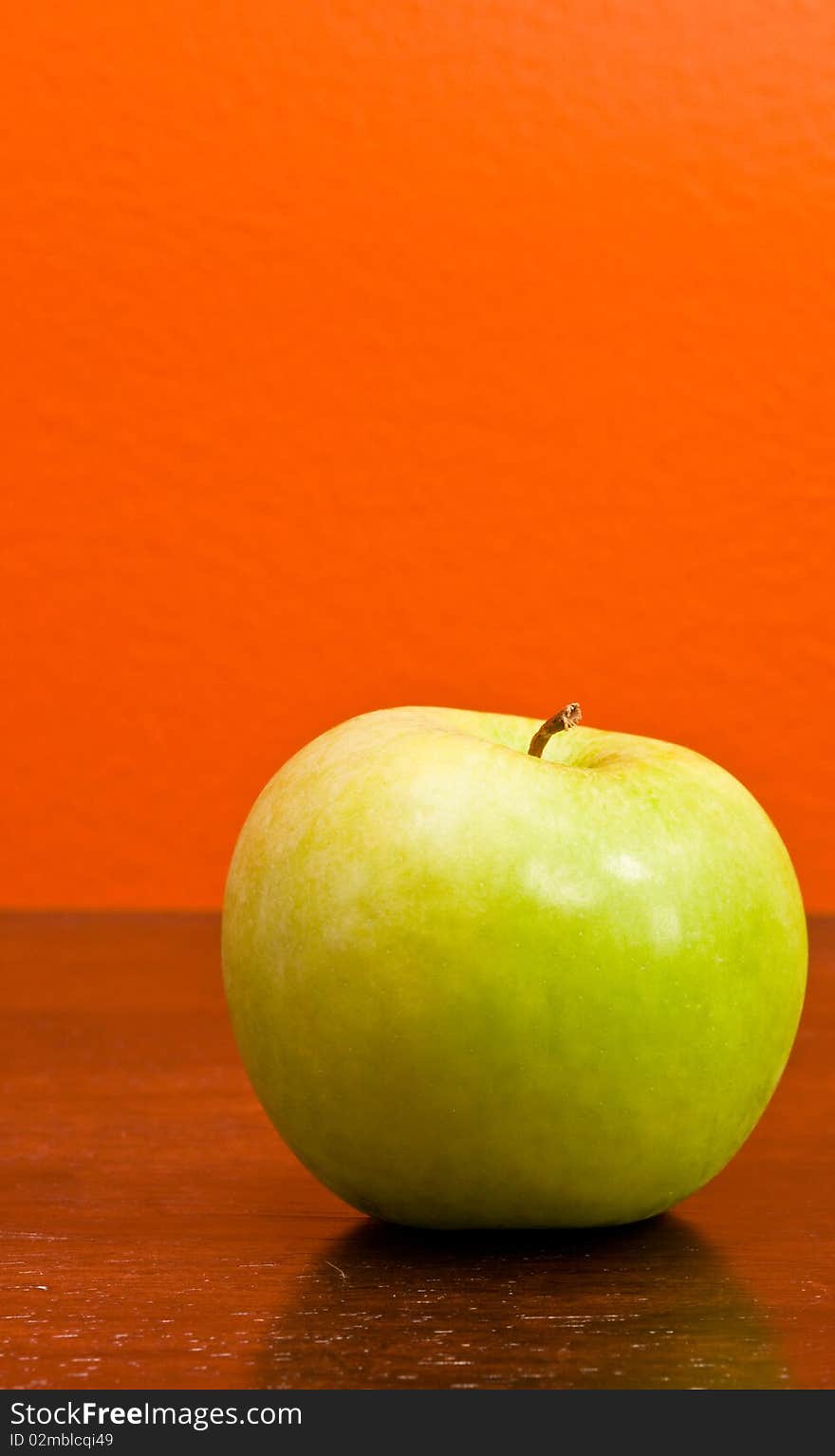 A delicious ripe green apple against an orange background. A delicious ripe green apple against an orange background.