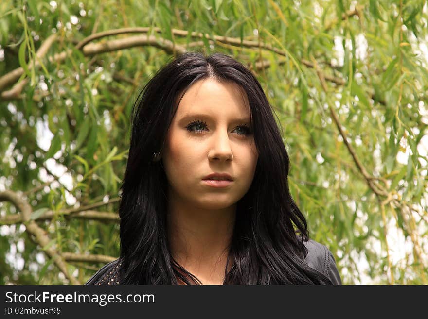 Attractive dark-haired young woman posing in front of a Willow tree. Attractive dark-haired young woman posing in front of a Willow tree