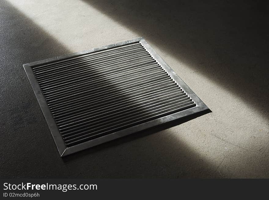 Steel grate in a concrete floor partially lit