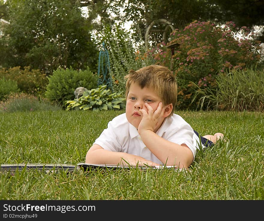 Young boy lays on grass dreaming while reading a book. Young boy lays on grass dreaming while reading a book