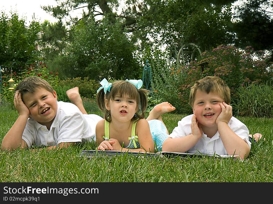 Brothers and sister laying on grass reading a book. Brothers and sister laying on grass reading a book