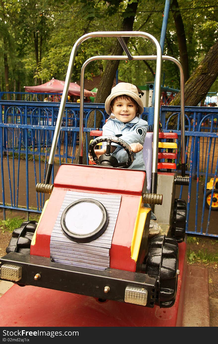 Little joyful boy in hat riding on toy-car on adventure playground, outdoor shot. Little joyful boy in hat riding on toy-car on adventure playground, outdoor shot