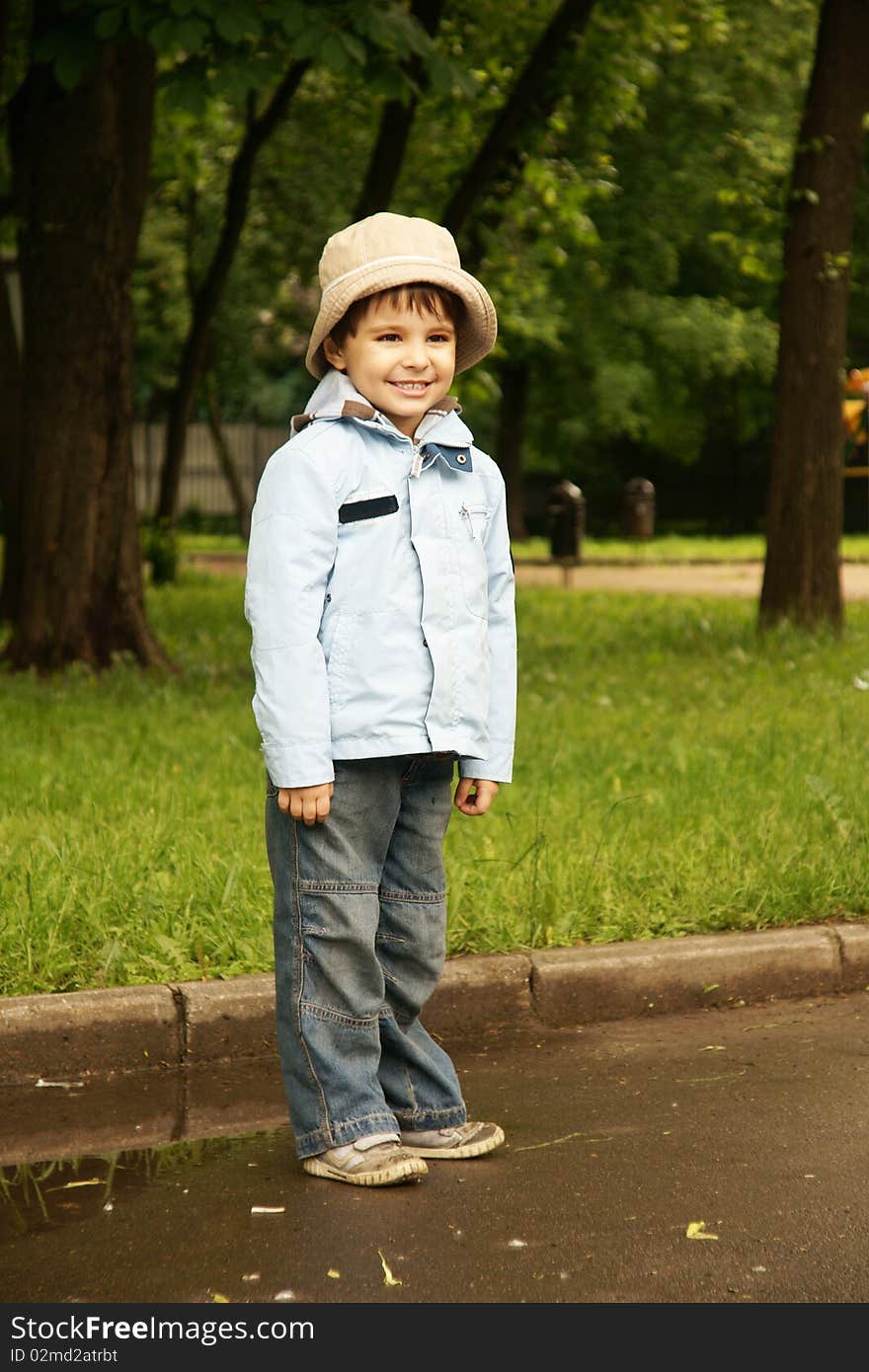 Little cute joyful boy in hat and blue jacket, outdoor shot