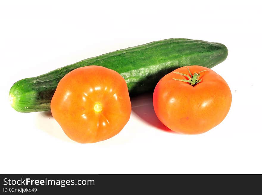 In the photo isolated on a white background is a vegetable cucumber and two tomatoes. In the photo isolated on a white background is a vegetable cucumber and two tomatoes.