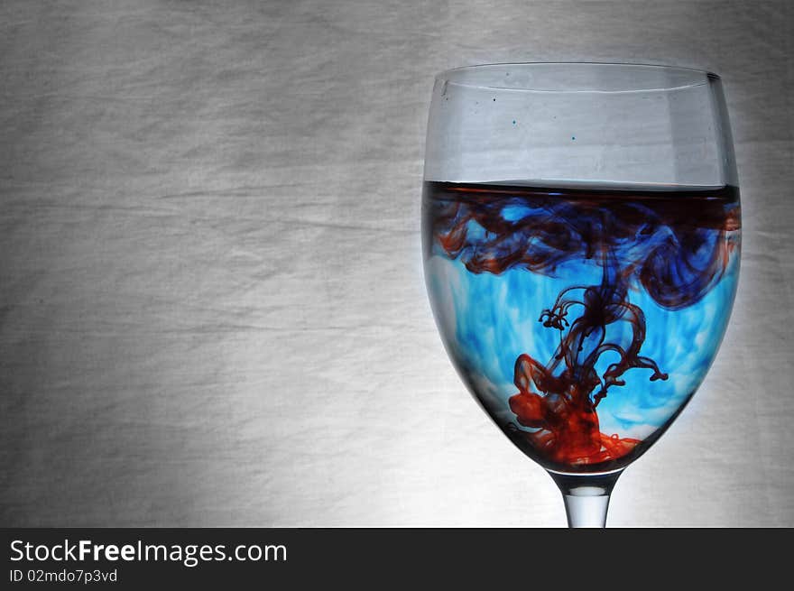 A drop of blue and red liquid was just poured into a clear wine glass. A drop of blue and red liquid was just poured into a clear wine glass.