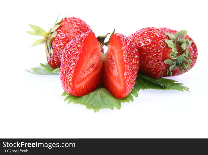 Strawberries on a leaf, one cut in half, on white background