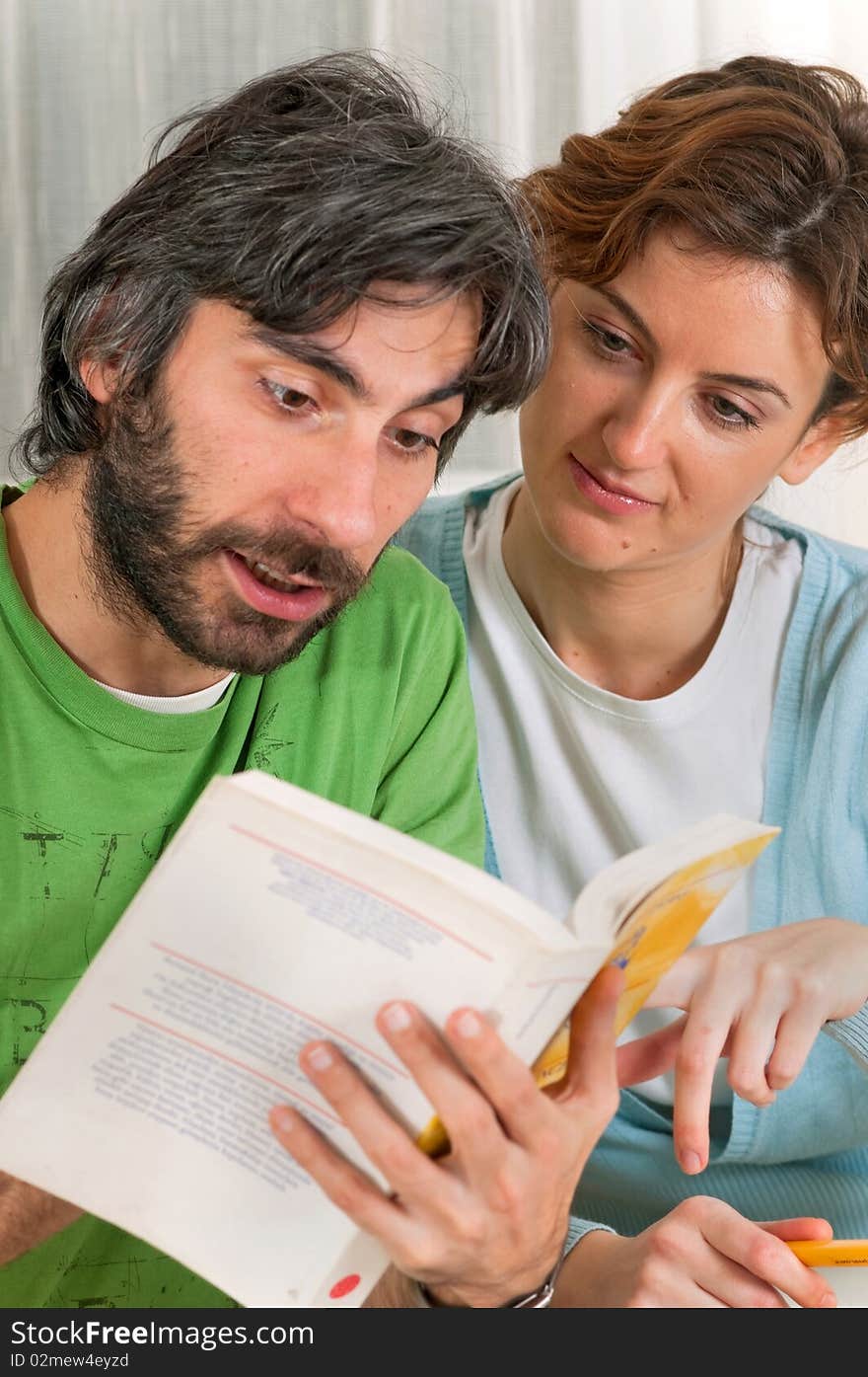 A young couple are sitting down reading a book together. The book is yellow and their clothing is pastel blue and green. A young couple are sitting down reading a book together. The book is yellow and their clothing is pastel blue and green.