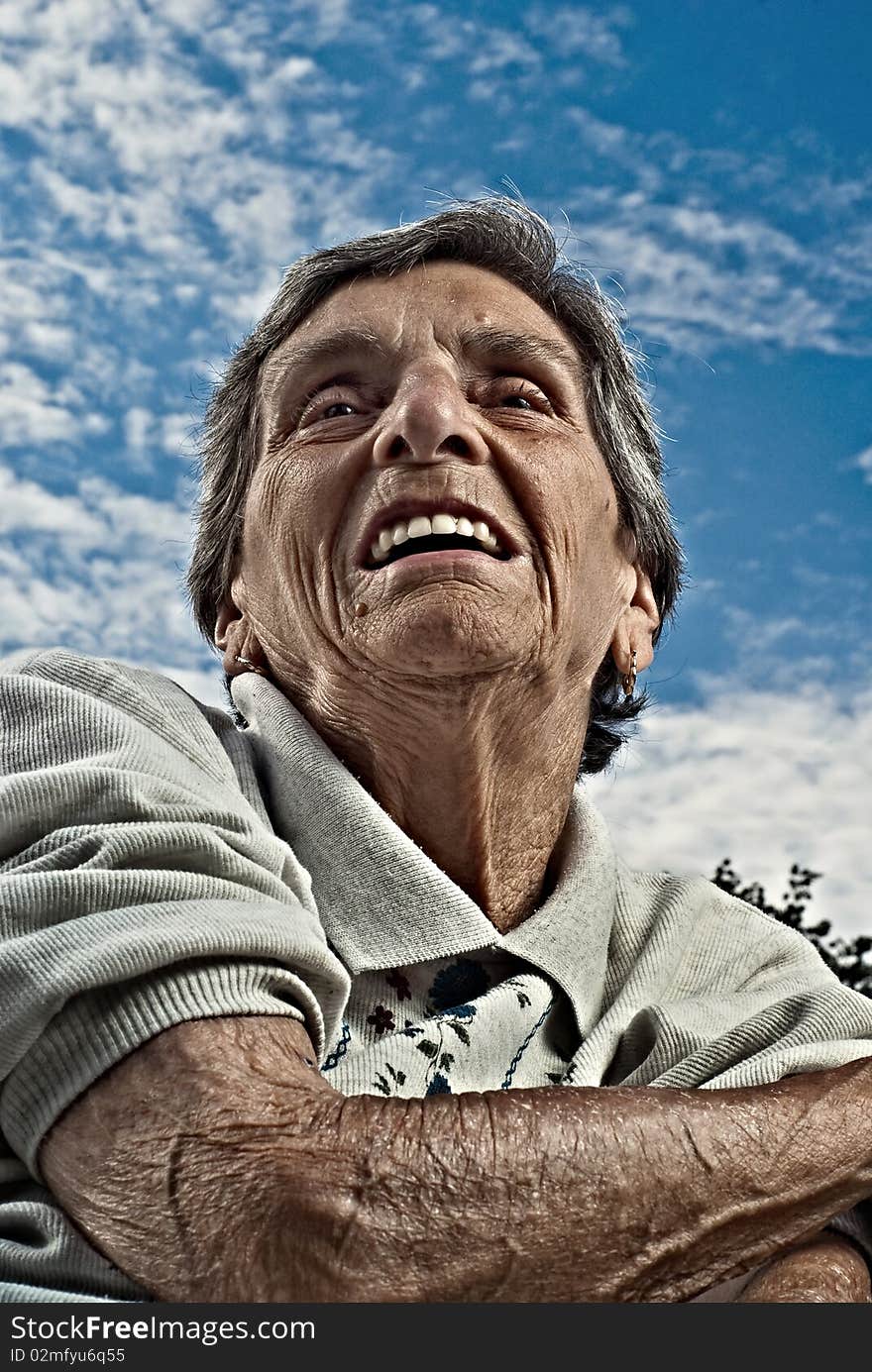 A closeup perspective portrait shot of a happy, elderly senior woman against a cloudy blue sky. A closeup perspective portrait shot of a happy, elderly senior woman against a cloudy blue sky.