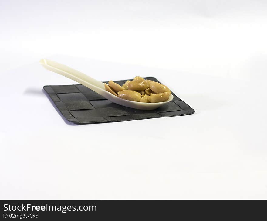 A spoonful of roasted, salted peanuts sitting in a spoon on a thatched mat. A spoonful of roasted, salted peanuts sitting in a spoon on a thatched mat.